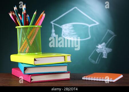 Metal cap of crayons with notebooks and bachelor hat drawing on blackboard background Stock Photo