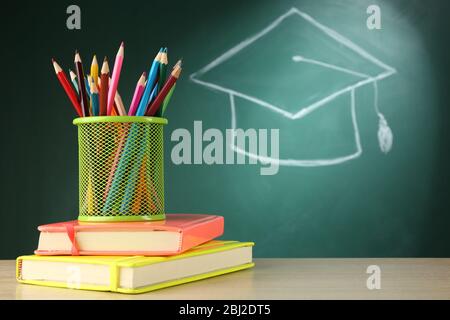 Metal cap of crayons with stack of books and bachelor hat drawing on blackboard background Stock Photo