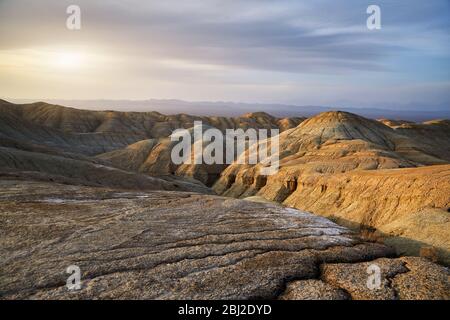 Cracked earth and bizarre layered mountains at sunset in desert park Altyn Emel in Kazakhstan Stock Photo