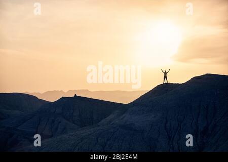 Man with rising hands in silhouette running on the mountains in the desert at sunset Stock Photo