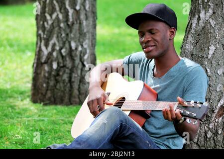 Handsome African American man with guitar sitting in park Stock Photo