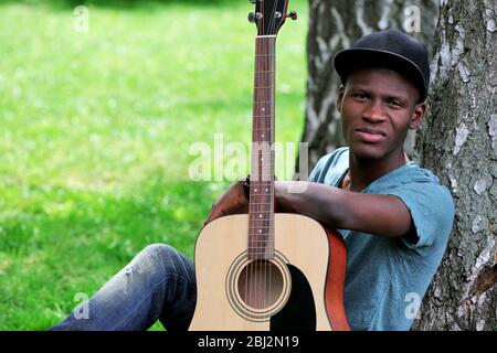Handsome African American man with guitar sitting in park Stock Photo