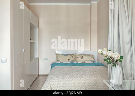 Cozy hotel room for two people. Small beige bedroom with bed and wardrobe. Stock Photo