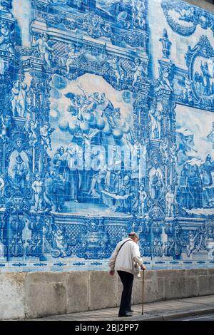 Man with walking cane passes azulejos Portuguese blue and white wall tiles of Capela das Almas de Santa Catarina  - St Catherine's Chapel in Porto, Po Stock Photo