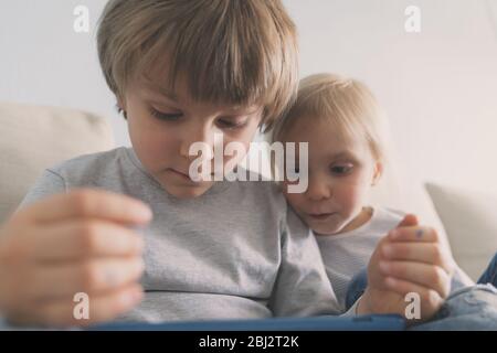 Two kids using tablet on sofa at home Stock Photo