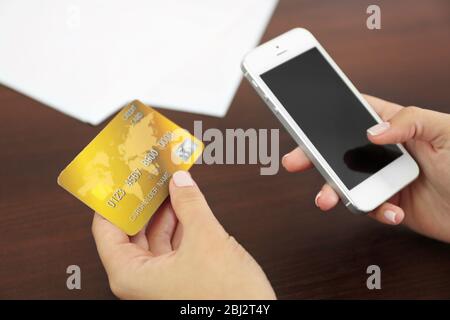 Woman verifies account balance on smartphone with mobile banking application on wooden table background Stock Photo