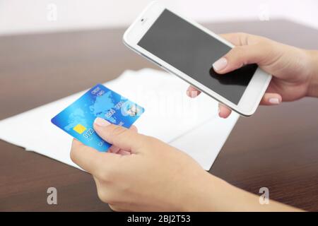 Woman verifies account balance on smartphone with mobile banking application on wooden table background Stock Photo