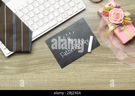 Happy father's day message on chalkboard. Flat lay composition on  working desk with computer keyboard, tie and gift boex. Stock Photo