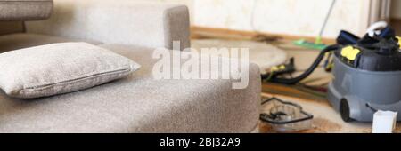 Sofa standing at domestic room with professional vacuum cleaner in background Stock Photo