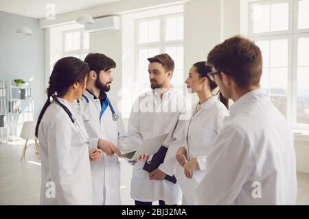 Group of practicing doctors in a meeting discuss the diagnosis of a patient standing in a clinic office. Stock Photo