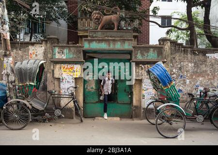 Dhaka / Bangladesh - January 14, 2019: young boy student with backpack exiting metallic tiny door in a street full of tuk tuk Stock Photo