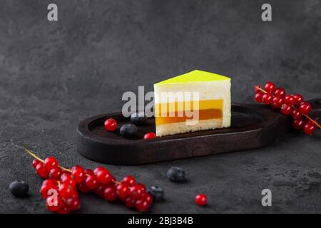 Piece of souffle lemon cake on wooden plate, with blueberry and red currant Stock Photo