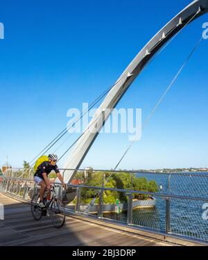 Male cyclistriding bike over the Elizabeth Quay Bridge a pedestrian bridge at Elizabeth Quay Perth foreshore on Swan River Western Australia. Stock Photo