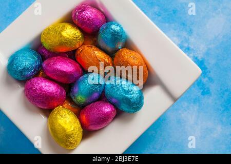 solid milk chocolate mini Easter eggs foil wrapped in bowl on blue patterned background - looking down on from above Stock Photo