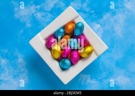 solid milk chocolate mini Easter eggs foil wrapped in bowl on blue patterned background - looking down on from above Stock Photo