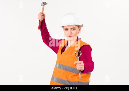 Feminism concept. Woman with strict face holds hammer, isolated on white background. Young woman works with tools as builder, copy space. Girl in helmet or hard hat going to crash with hammer. Stock Photo