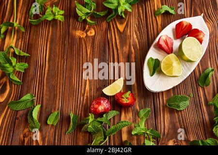 cooking of cooling summer cocktail with strawberries, ice and mint and around the berries are ripe fresh strawberries and lime Stock Photo