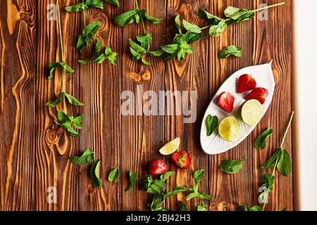 cooking of cooling summer cocktail with strawberries, ice and mint and around the berries are ripe fresh strawberries and lime Stock Photo