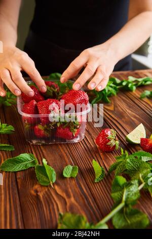 cooking of cooling summer cocktail with strawberries, ice and mint and around the berries are ripe fresh strawberries and lime Stock Photo