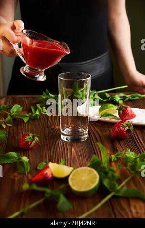 cooking of cooling summer cocktail with strawberries, ice and mint and around the berries are ripe fresh strawberries and lime Stock Photo