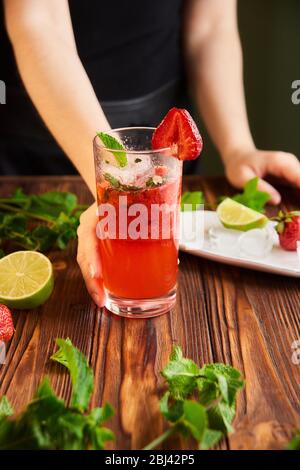 cooking of cooling summer cocktail with strawberries, ice and mint and around the berries are ripe fresh strawberries and lime Stock Photo