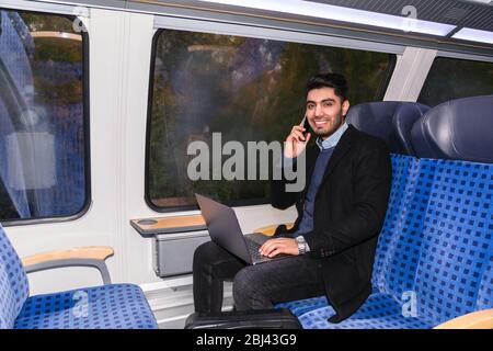 Man sits in train, holds laptop and talks on phone Stock Photo