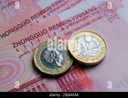 One pound coins placed on top of 100 Chinese yuan renminbi banknotes. Photographed with selective focus. Words in different languges translate as 'The Stock Photo