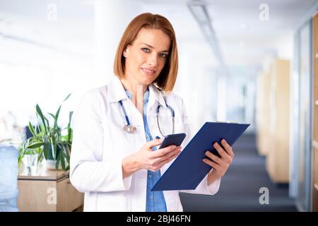 Shot of middle aged female doctor text messaging while standing in medical clinic. Stock Photo