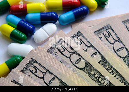 Pile of pills of different colours such as blue, yellow, red and white placed next to 50 dollar bills. Illustrative for cost of medical bills, health Stock Photo