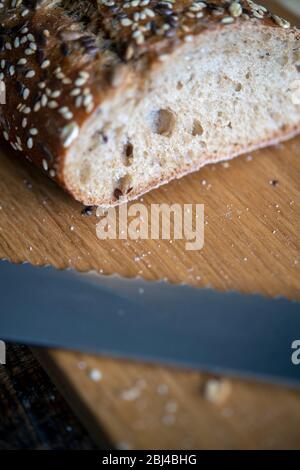 Freshly baked seeded loaf and bread knife on a cutting board Stock Photo