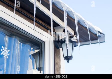 Window with a snowflake glued on the glass, a little lantern, icicles hanging from the roof Stock Photo