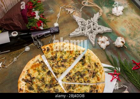 Pizza with mushrooms and cheese on a festive table, sprinkled with dry Italian herbs. Against the background of New Year's toys Stock Photo