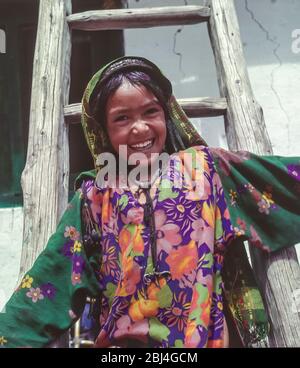 Pakistan, Northern Areas of the Karakoram Mountains. A young girl in colourful dress  poses for the camera in the Baltistan village of Hushe Stock Photo