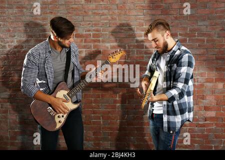 Young men playing guitars on brick wall background Stock Photo