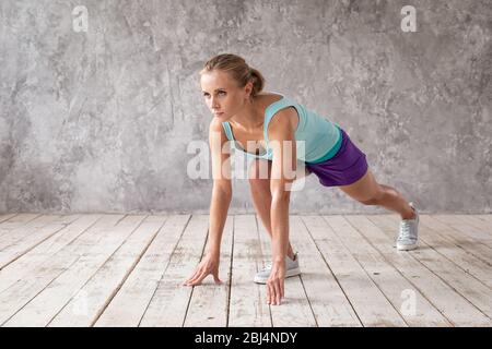 Sporty blond woman doing lunges with her arms touching wooden floor. Stock Photo