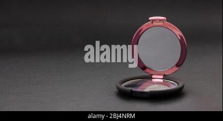 Make up mirror against black background, closeup view, copy space. Small pocket mirror round shape, double in shiny pink color Stock Photo