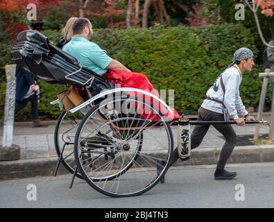 A young rickshaw driver is pulling two tourists in Arashiyama, Kyoto, Japan Stock Photo