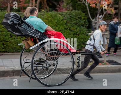 A young rickshaw driver is pulling two tourists in Arashiyama, Kyoto, Japan Stock Photo