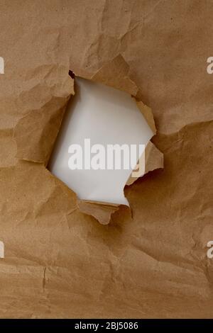 Vertical shot frame in the form of a torn hole of brown paper with a white inner layer of the window. Stock Photo