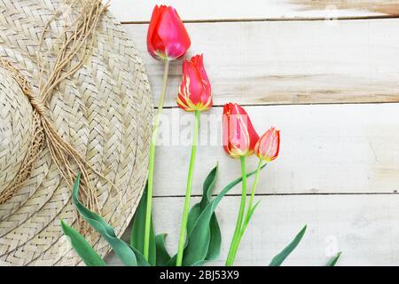 Red and yellow striped tulips and straw hat on wooden table Stock Photo