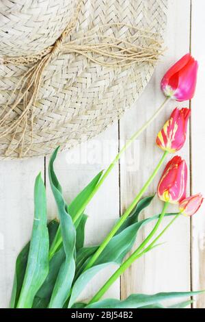 Red and yellow striped tulips and straw hat on wooden table Stock Photo