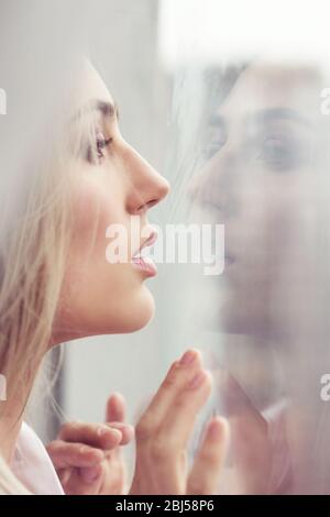 Beautiful young woman standing near the window. Reflection in the window. Stock Photo