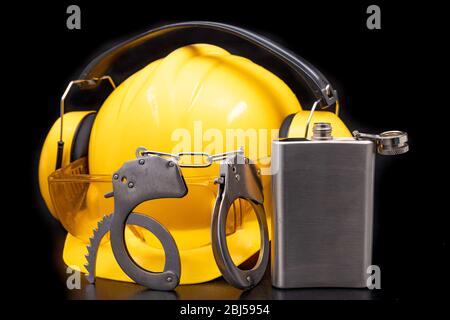 Construction helmet, handcuffs and vodka in a bottle. Drunkenness at work in the responsible position of engineer. Dark background. Stock Photo