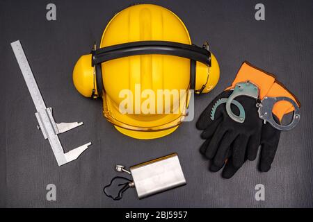 Construction helmet, handcuffs and vodka in a bottle. Drunkenness at work in the responsible position of engineer. Dark background. Stock Photo
