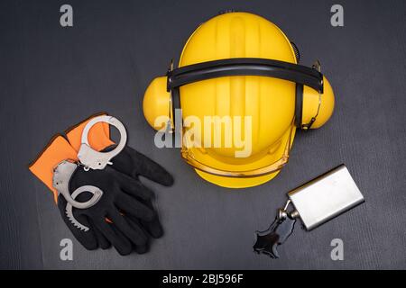 Construction helmet, handcuffs and vodka in a bottle. Drunkenness at work in the responsible position of engineer. Dark background. Stock Photo