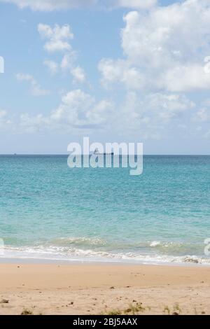 Photo taken of the beach in portrait orientation on a bright sunny day with a cargo vessel in the background out on the horizon Stock Photo