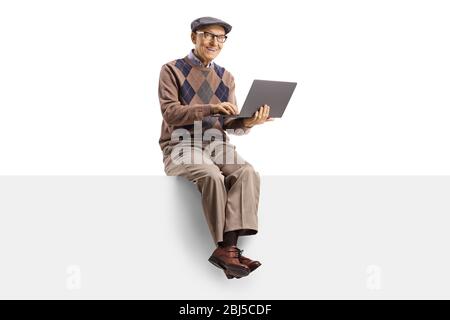 Elderly man sitting on a blank panel and using a laptop computer isolated on white background Stock Photo