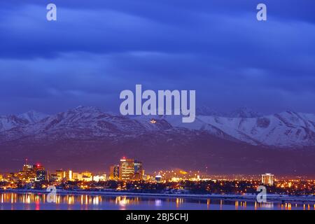 Anchorage Alaska skyline during blue hour with Chugach mountains in background viewed across Cook inlet from Earthquake park in winter.