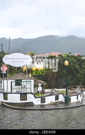 Furnas, Azores, Portugal - Jan 13, 2020: Village street by volcanic hot springs in Portuguese Furnas. Geothermal sulfur spring. Steam coming from the water pools. Houses and hills in the background. Stock Photo