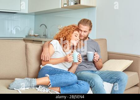 Relationship Concept. Couple sitting on sofa at living room hugging drinking hot coffee happy and relaxed Stock Photo